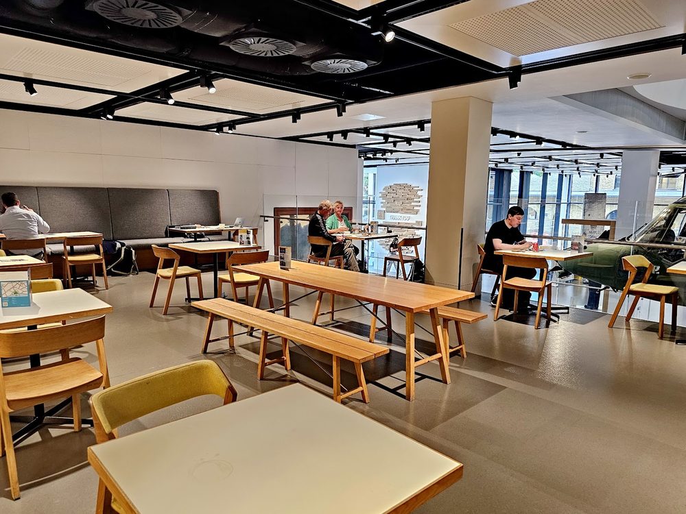 Pale wood tables and chairs under the open industrial ceiling of the cafe