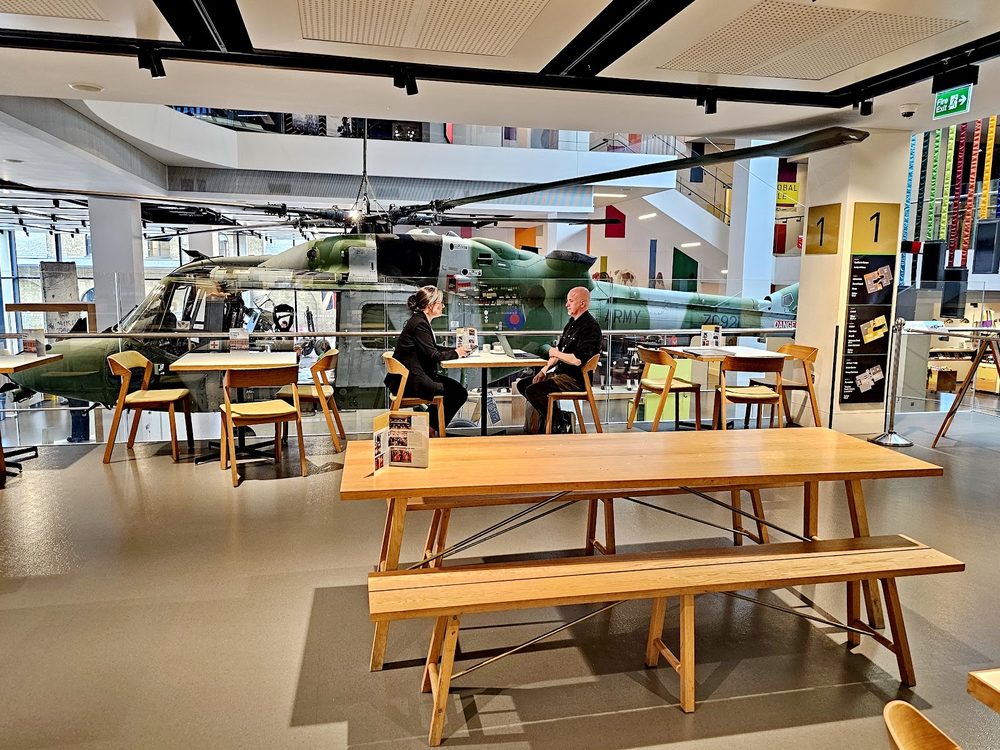The cafe's long bench tables with the museum's aircraft exhibit visible through the glass behind