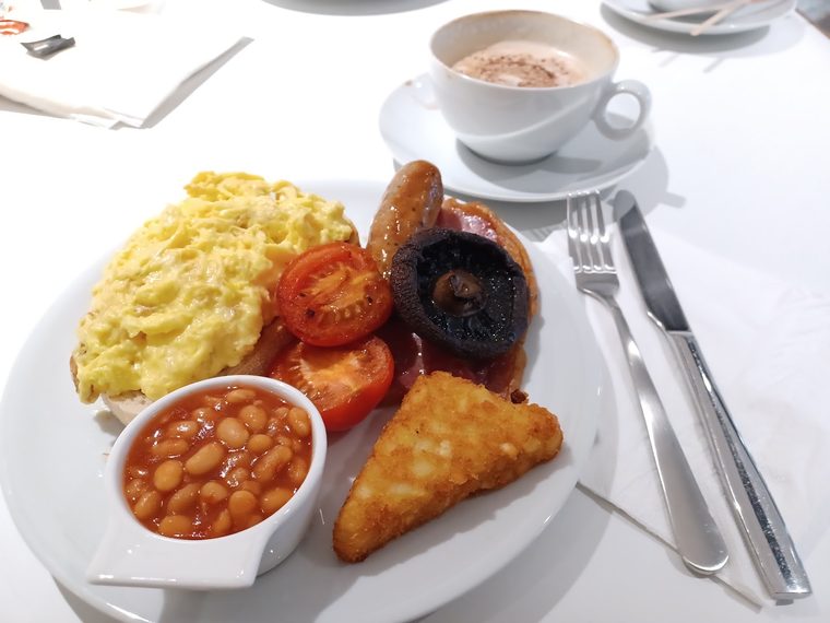 A cooked breakfast of egg, sausage, tomatoes, black pudding, hash browns and beans